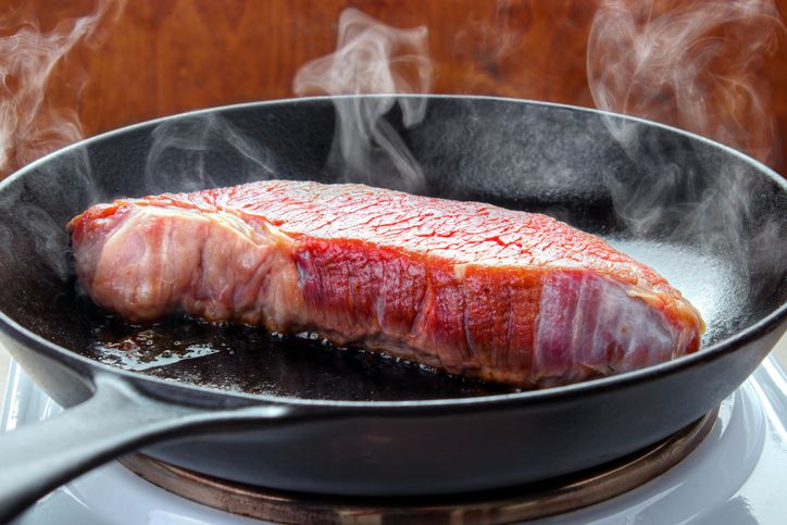 Searing beef brisket steak on the electric stove with hot cast iron skillet