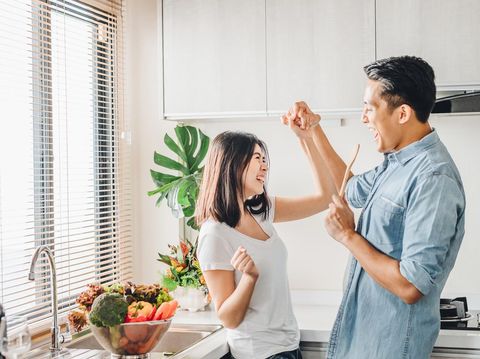 Romantic Asian couple in love is dancing and smiling while cooking together in kitchen