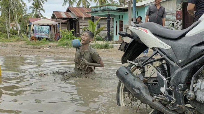 Warga melakukan aksi mandi lumpur dan mencuci sepeda motor di kubangan jalan rusak di Asahan. (Istimewa)
