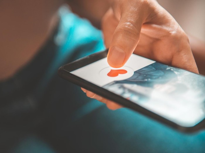 Finger of woman pushing heart icon on screen in mobile smartphone application. Online dating app, valentines day concept.