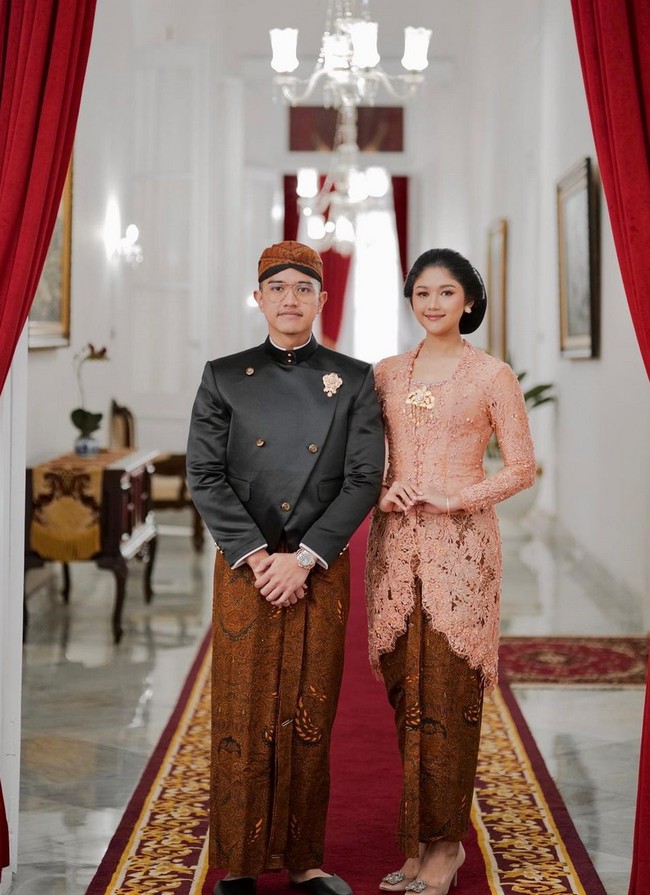Erina Gudono mengenakan kebaya klasik bernuansa peach saat berpose bersama Kaesang Pangarep di Istana Negara. Kebaya rancangan Wiranti Kurnia ini dipadukan dengan kain batik wiron. Finalis Puteri Indonesia 2022 ini pun memakai sanggul Jawa klasik yang anggun. Foto: Instagram/@erinagudono