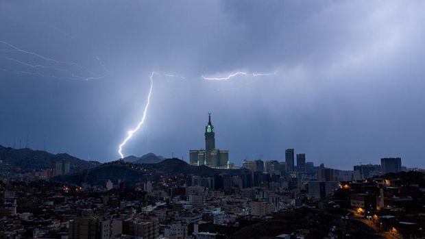 Sebuah gambar yang diambil pada 22 Agustus 2023 menunjukkan petir di atas menara jam Mekkah di Arab Saudi. Badai dahsyat menutup sekolah-sekolah pada tanggal 23 Agustus di wilayah Mekah di kerajaan gurun pasir, tempat Masjidil Haram berada, yang dilanda hujan lebat dan angin semalaman, kata para saksi mata. (Hammad Al-Huthali / AFP)