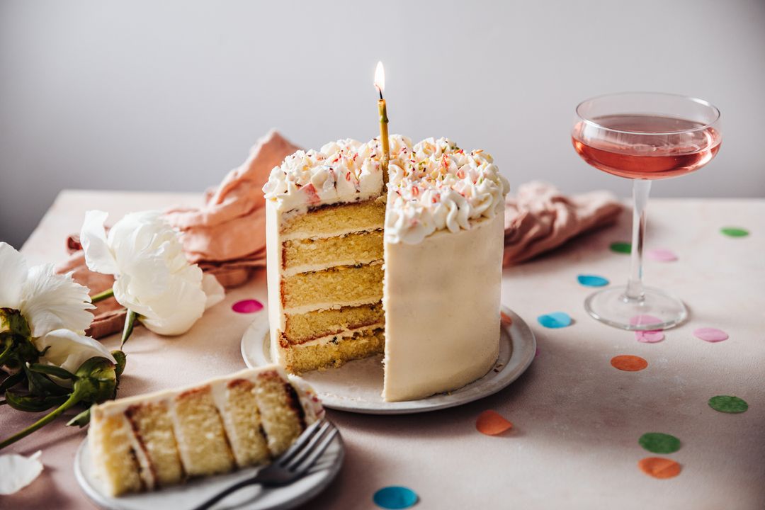 Homemade layered cake decorated with cheese cream icing and multi colored sugar sprinkles. Beautiful birthday cake with candle on a table.