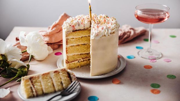 Homemade layered cake decorated with cheese cream icing and multi colored sugar sprinkles. Beautiful birthday cake with candle on a table.