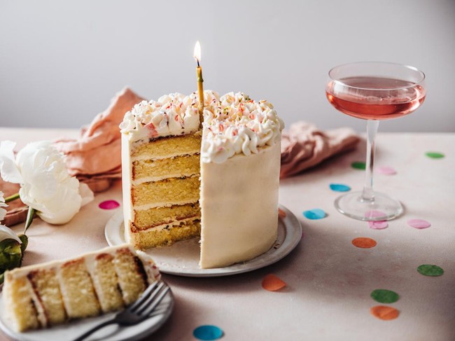 Homemade layered cake decorated with cheese cream icing and multi colored sugar sprinkles. Beautiful birthday cake with candle on a table.