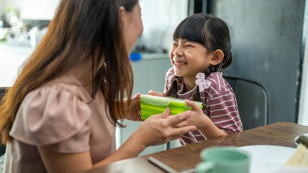 Image of Asian mother making healthy school lunch box for her daughter. Mother giving her daughter the healthy sandwich.
