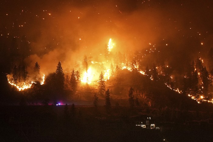 The McDougall Creek wildfire burns on the mountainside above a lakefront home in West Kelowna, B.C., on Friday, August 18, 2023. (Darryl Dyck/The Canadian Press via AP)