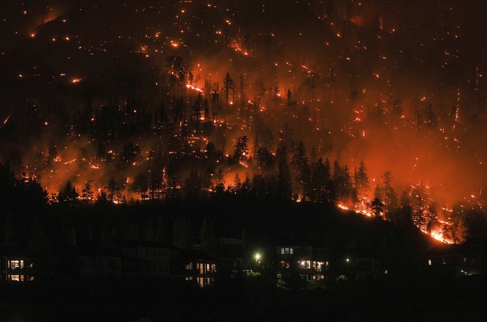The McDougall Creek wildfire burns on the mountainside above a lakefront home in West Kelowna, B.C., on Friday, August 18, 2023. (Darryl Dyck/The Canadian Press via AP)