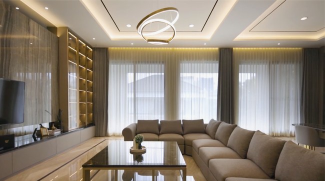 Ruang keluarga yang luas dilengkapi sofa panjang yang dapat mengakomodasi banyak orang. Fitur mood lighting di langit-langit semakin menciptakan atmosfer yang hangat saat berkumpul. (Foto: YouTube/DMC Architect & Interior Studio)