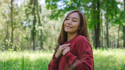Portrait image of a young woman with closed eyes putting hands on her chest in the park