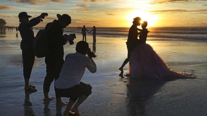 Bali Dinobatkan Sebagai Lokasi Sunset Terbaik di Dunia, Nih Potretnya FILE- In this Jan. 18, 2017, file photo, photographers take photos of a tourist couple's wedding at the famous Kuta beach during sunset in Bali, Indonesia. According to a 2016 survey from wedding site The Knot, the average cost of an international destination wedding is $25,800. That figure may be within your event budget, but for guests, international airfare and multinight lodging could be out of reach. (AP Photo/Firdia Lisnawati, File)