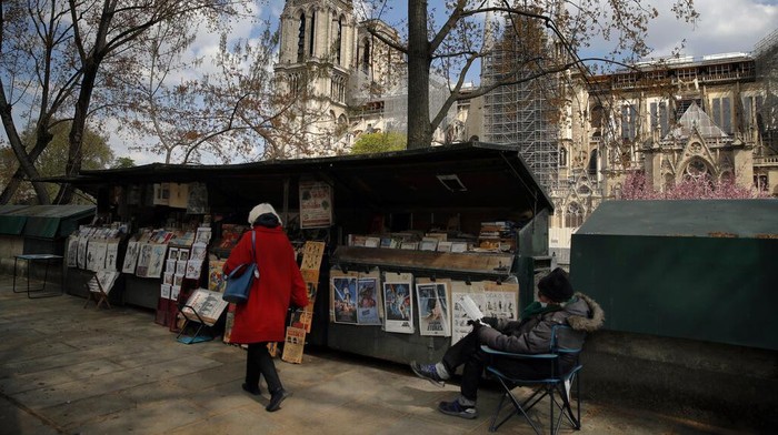 Kios Buku Tua Warisan UNESCO di Sepanjang Sungai Seine Paris Bakal Digusur A woman walks by a booksellers called