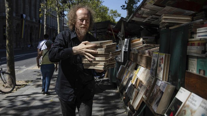 Kios Buku Tua Warisan UNESCO di Sepanjang Sungai Seine Paris Bakal Digusur Jerome Callais, head of the Paris Booksellers' Cultural Association, carries books at his bookseller booth along the Seine Riverbank in Paris, Tuesday, Aug. 22, 2023. The host city of Paris vowed to deliver an extraordinary grand opening on July 26, 2024, as the ceremony is expected to draw about 600,000 spectators to the Parisian quayside. Citing security measures, the Paris police prefecture ordered on July 25 the removal of 570 stationary boxes out of which booksellers have operated for decades on the quays of the Seine river. (AP Photo/Sophie Garcia)