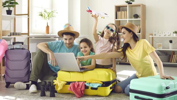 Happy excited family and daughter children buying payment for flight ticket booking hotel online using laptop with travel suitcase around at home living room. Holiday vacation traveling abroad concept