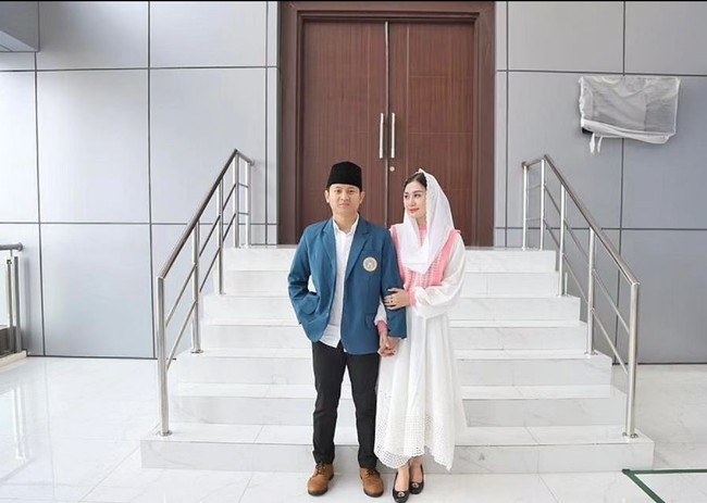 Pose bersama suami, ibu dua anak ini memadukan kemeja, rok bersiluet handkerchief dan outerwear berupa vest pink paste. Sementara kerudungnya senada dengan busana berwarna putih. Foto: Instagram/@novitamochamad