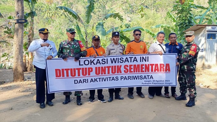 Petugas saat membentangkan spanduk bertuliskan penutupan sementara Selopamioro Adventure Park di Imogiri, Bantul.