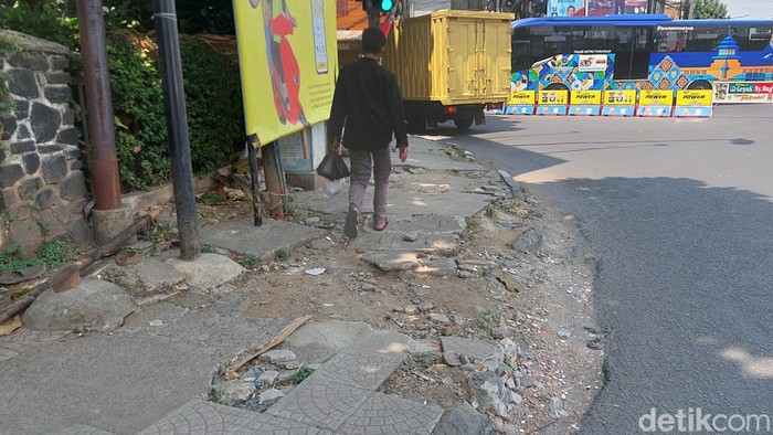Warga berjalan di atas trotoar yang rusak.