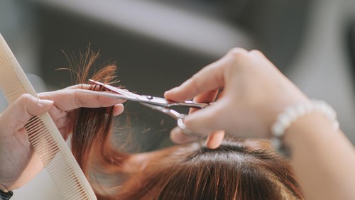 close up Asian chinese female hairstylist hairdresser cutting hair for her customer in hair salon