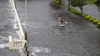 Warga asyik mengayuh board-nya di jalanan yang terendam banjir. AP Photo/Chris OMeara.  
