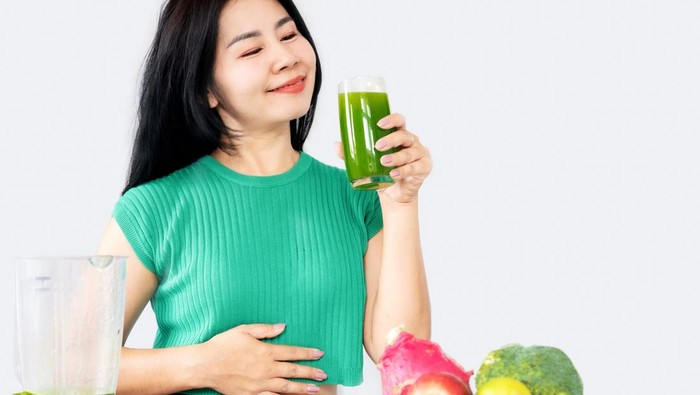 healthy Asian woman drinking mix of green vegetables and fruit juice for detox and diet