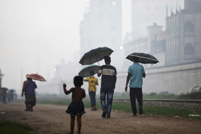 People sit on a rail track as smoke rises from steel mills near a slum in Dhaka, Bangladesh August 29, 2023. REUTERS/Mohammad Ponir Hossain