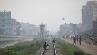 Orang-orang duduk di rel kereta api saat asap mengepul dari pabrik baja dekat daerah kumuh di Dhaka, Bangladesh 29 Agustus 2023. Dhaka jadi salah satu kota yang paling buruk kualitas udaranya di dunia belakangan bersaing ketat dengan Jakarta.