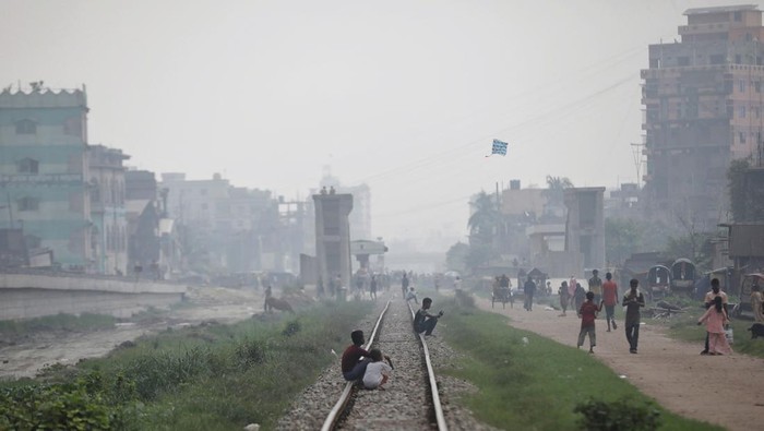 People sit on a rail track as smoke rises from steel mills near a slum in Dhaka, Bangladesh August 29, 2023. REUTERS/Mohammad Ponir Hossain
