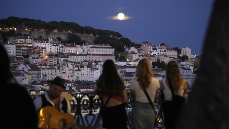 People watch a supermoon rise above Lisbon, Wednesday, Aug. 30, 2023. Its the months second supermoon, when a full moon appears a little bigger and brighter thanks to its slightly closer position to Earth. (AP Photo/Armando Franca)