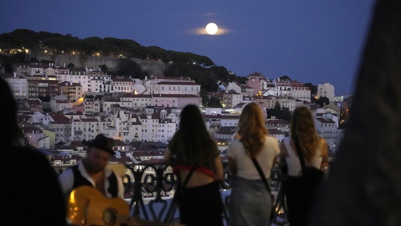 People watch a supermoon rise above Lisbon, Wednesday, Aug. 30, 2023. It's the month's second supermoon, when a full moon appears a little bigger and brighter thanks to its slightly closer position to Earth. (AP Photo/Armando Franca)