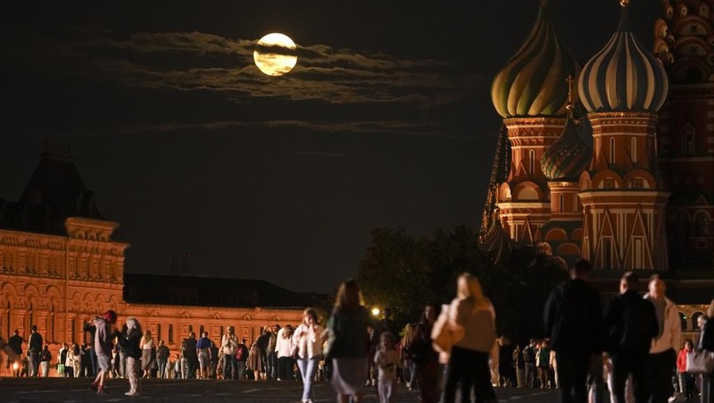 The August Super Blue Moon sets behind a historical building and the St. Basil's Cathedral, right, as people walk in Red Square in Moscow, Russia, Wednesday, Aug. 30, 2023. The cosmic curtain rises Wednesday night with the second full moon of the month, the reason it is considered blue. It is dubbed a supermoon because it is closer to Earth than usual, appearing especially big and bright. (AP Photo/Alexander Zemlianichenko)