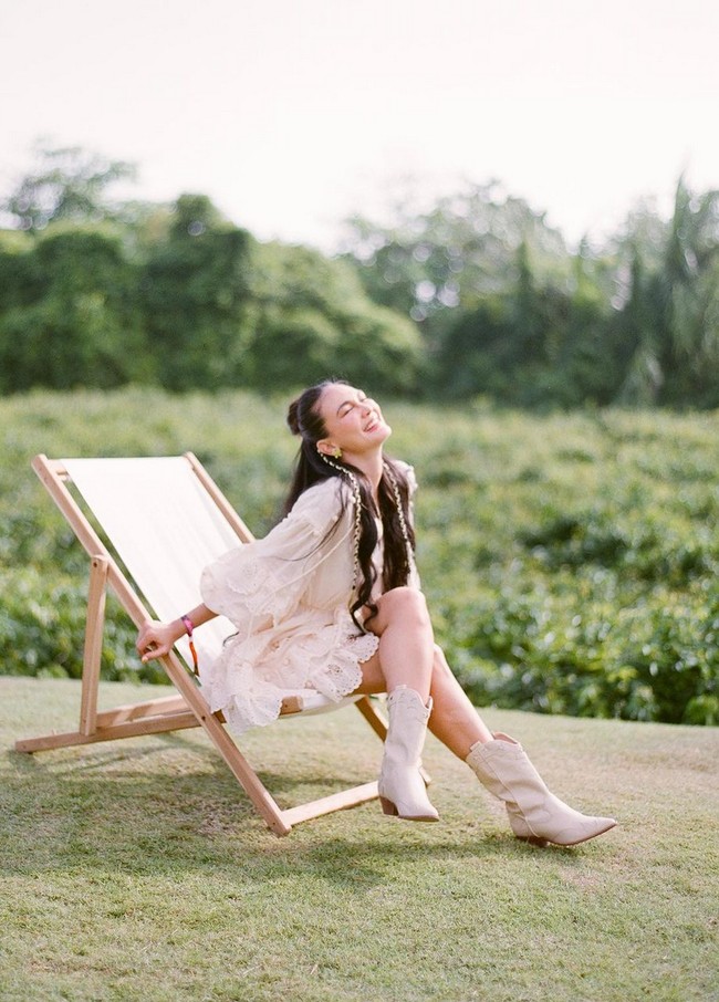 Luna Maya mengenakan mini dress warna ivory dengan detail lace dan pom pom. Dia memadukan busana dengan boots warna senada. Foto: Instagram/@lunamaya