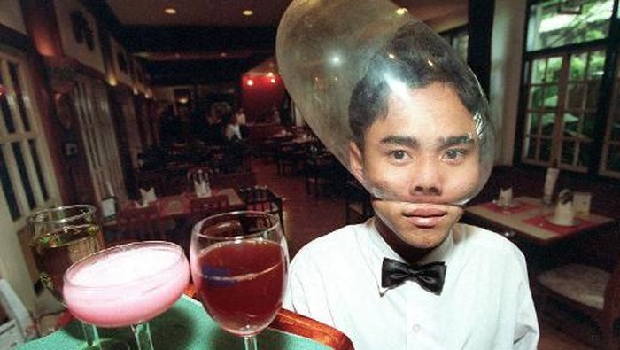 Seorang pelayan di restoran Cabbages & Condoms di Bangkok menyajikan minuman dengan menggunakan kondom di atas kepalanya.