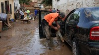 Seorang warga mencoba membersihkan sisa lumpur dari mobilnya akibat banjir yang menerjang wilayah tersebut.