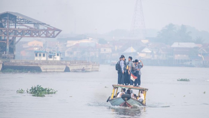 Sejumlah pelajar berangkat sekolah menggunakan perahu tradisional melewati kawasan yang diselimuti kabut asap di Sungai Ogan, Palembang, Sumatera Selatan, Rabu (6/9/2023). Kabut asap tersebut merupakan dampak dari kebakaran hutan dan lahan yang terjadi diberbagai Kabupaten yang ada di Provinsi Sumatera Selatan. ANTARA FOTO/Nova Wahyudi/tom.