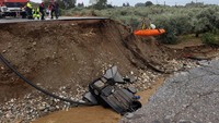 Sebuah mobil masuk ke sungai setelah jembatannya roboh. Sementara di atasnya petugas pengevakuasi warga dengan tali. 
