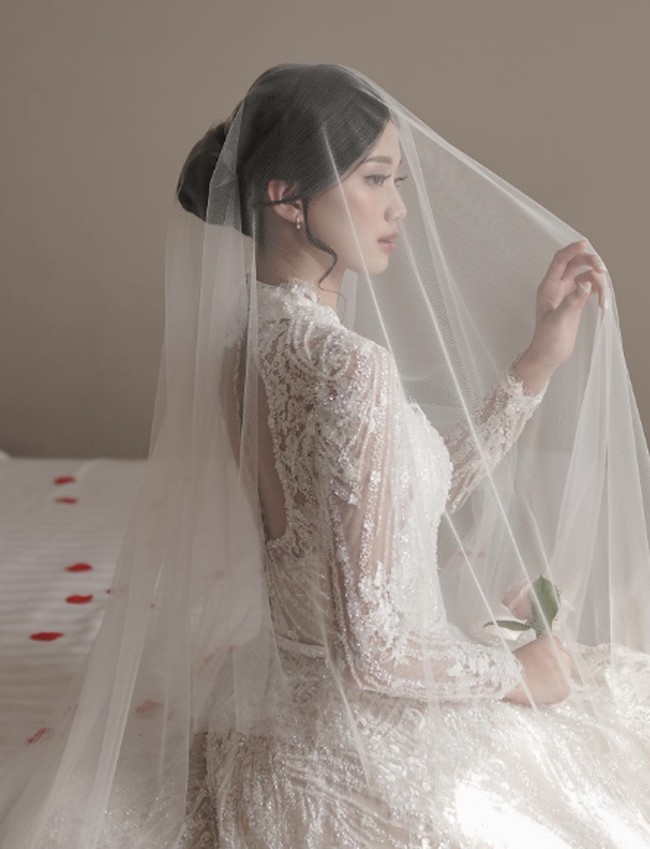 Desy Genoveva eks JKT48 tampil lebih sederhana tapi elegan ketika upacara pemberkatan. Ia mengenakan gaun pengantin berpayet lengan panjang yang transparan pada bagian lengan.  Foto: Instagram @desygenoveva_/dok. Wedding Factory