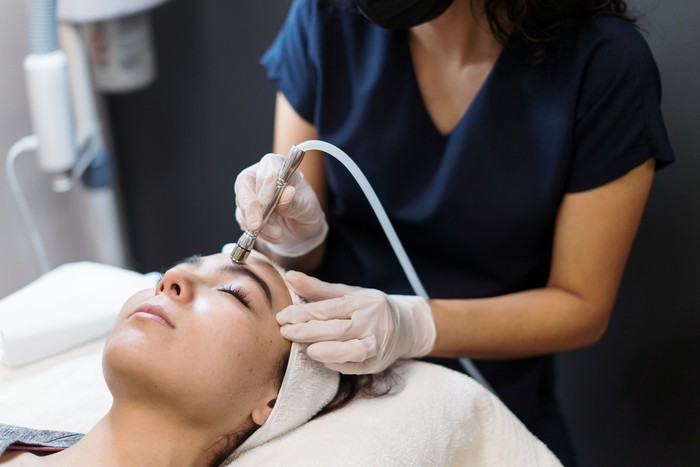 1372582333 A young latin woman getting a facial treatment with a device.