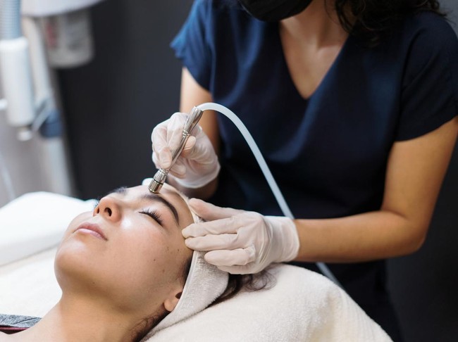 A young latin woman getting a facial treatment with a device.