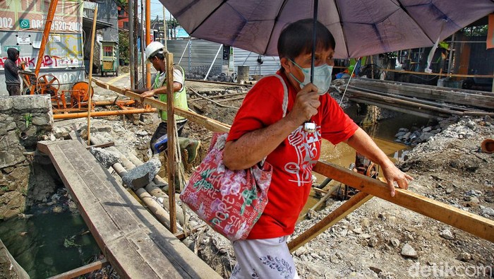 Warga berjalan kaki melintasi sungai dengan jembatan seadanya di samping proyek peninggian jembatan di Jl Ceger Raya, Pondok Aren, Tangerang Selatan, Jumat (8/9/2023).