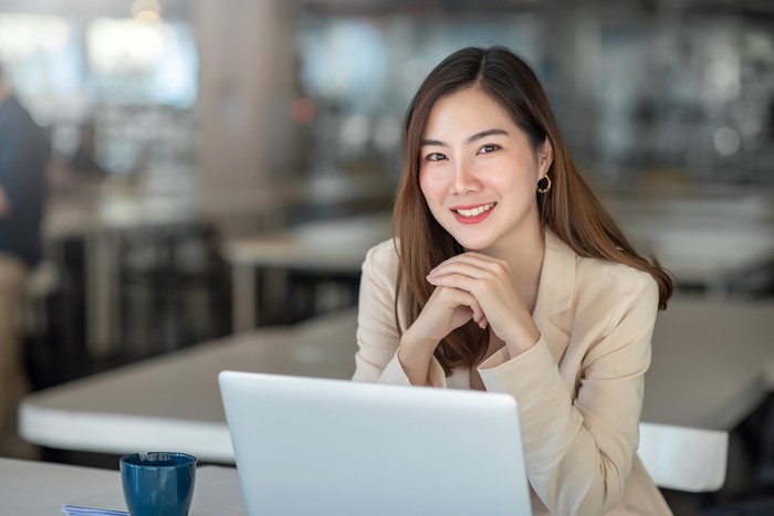 Charming Asian businesswoman working with a laptop at the office. Looking at camera.