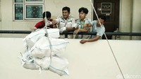 Warga dengan dibantu petugas menurunkan barang-barangnya dari atas rusun menggunakan tali.  
