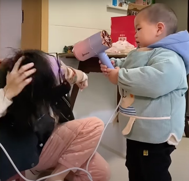 Mulai dari menyuapi ibunya makan, membantu mengeringkan rambut, hingga membersihkan rumah, semuanya bisa dikerjakan oleh Pomelo. Seperti yang terlihat dalam foto, saat Pomelo membantu memegang pengering rambut untuk ibunya. Foto: South China Morning Post