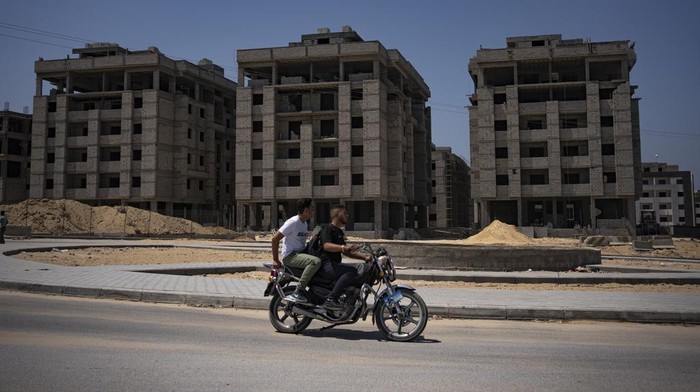 Palestinians on a motorcycle pass nearly completed Egyptian-funded residential buildings in northern Gaza Strip, Sunday, Aug. 27, 2023. Scores of displayed Palestinian families are awaiting completion of nearly 1,400 homes, but the project has become mired in political disputes between the Palestinian Authority and Gaza’s Hamas-run government.(AP Photo/Fatima Shbair)
