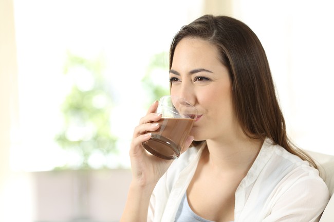 Happy woman drinking a cocoa shake sitting on a couch in the living room at home