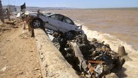 Sebagian mobil tersangkut beton pemecah ombak. Selain itu ada juga yang nangkring di atas tanggul pembatas laut di Kota Derna, Libya.  