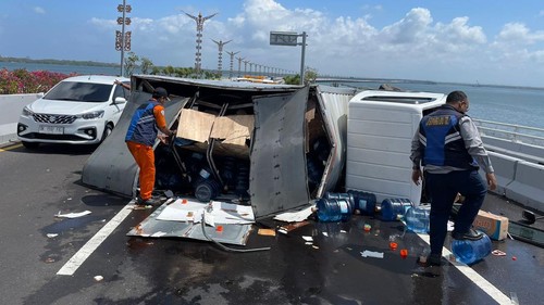 Mobil box berpelat nomor DK 8024 CP yang mengangkut ratusan galon air mineral terguling setelah mengalami pecah ban di Jalan Tol Bali Mandara, tepatnya di kilometer 3+600, Senin (18/9/2023).
