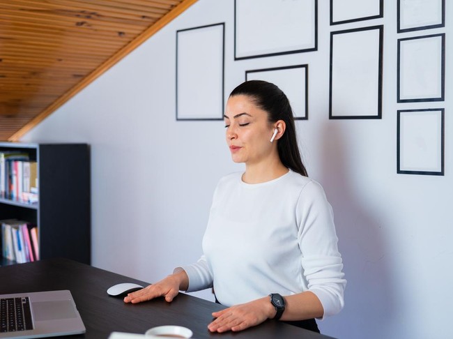 Relaxed calm business woman take deep breath of fresh air resting with eyes closed at work in home office. Doing office yoga and meditating with closed eyes.
