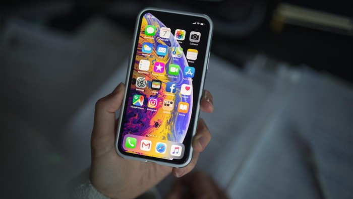 Celje, Slovenia - October 07, 2018: Woman holding new iPhone XS smartphone (with protective VRS design case, 5.8 inch Retina display, silver color version with 256 GB memory) in her hand over the note pad.