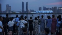 Orang-orang menunggu pertunjukan cahaya yang ditampilkan dari Hangzhou Olympic Sports Centre Stadium di sepanjang tepi sungai di Hangzhou, China, Selasa (19/9/2023). Pertunjukan cahaya tersebut dalam rangka menyambut Asian Games ke-19 di Hangzhou.  