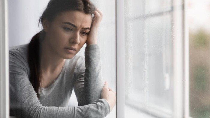 Unhappy sad european young lady suffering from depression, stress and mental problems near window with rain drops at home. Negative human emotions, despaired facial expression, reaction on bad news